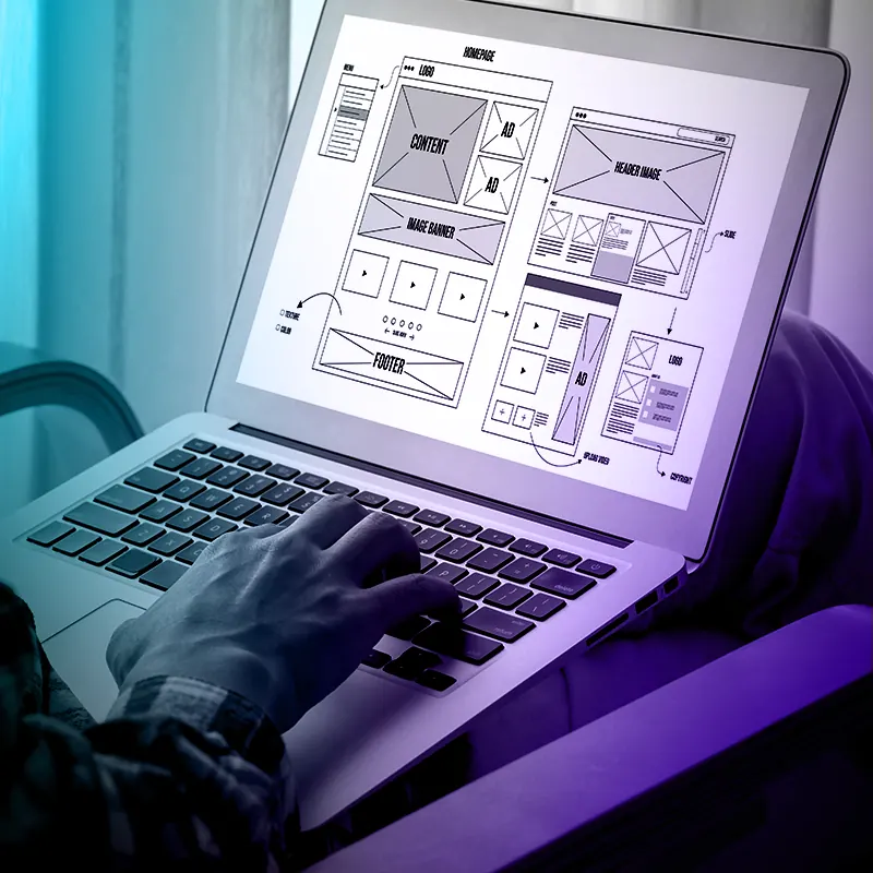 Mãos digitando em um notebook com o wireframe de um site na tela